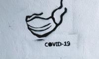 Sort grafitii på hvid væg af et mundbind og teksten: COVID-19