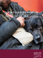 Billede af forsiden på årsrapport 2019: en mand med Hus-Forbi-key-hanger og sin hund på skødet. En støtte sort/brung hund.